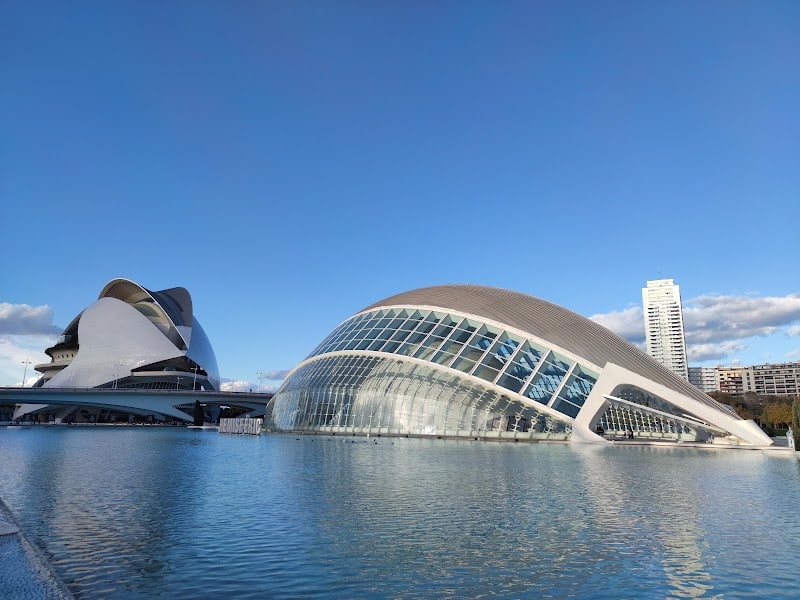 Futuristic buildings with curved, glass surfaces stand beside a reflective pool under a clear blue sky, creating scenes worthy of any travel map.