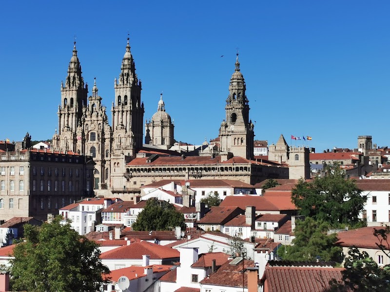 View of a historic cathedral with multiple spires, surrounded by red-roofed buildings under a clear blue sky, reminiscent of scenes found in a travel map.