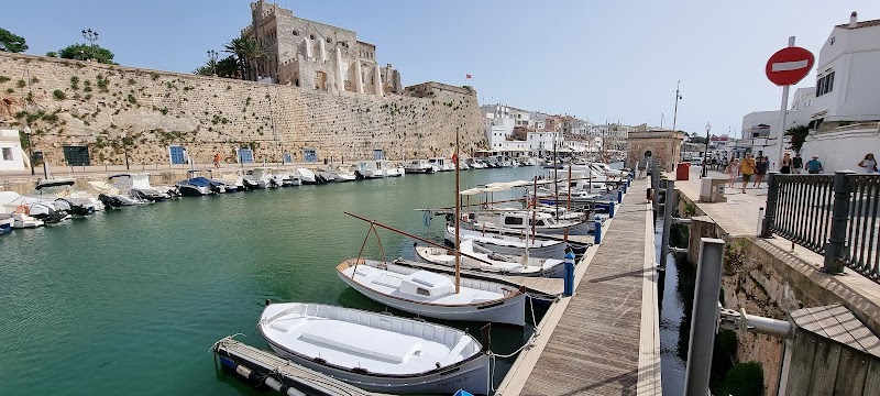 Boats are moored along a stone-lined canal with historic buildings and a stone wall in the background under a clear sky, waiting to be explored by travelers with a trusty tourist map.