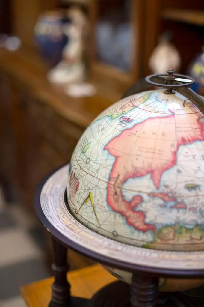 A vintage globe on a wooden stand, displaying part of North America and Asia, with blurred objects in the background. A vintage globe on a wooden stand, displaying part of North America and Asia, with blurred objects in the background NORTHAMERICA.